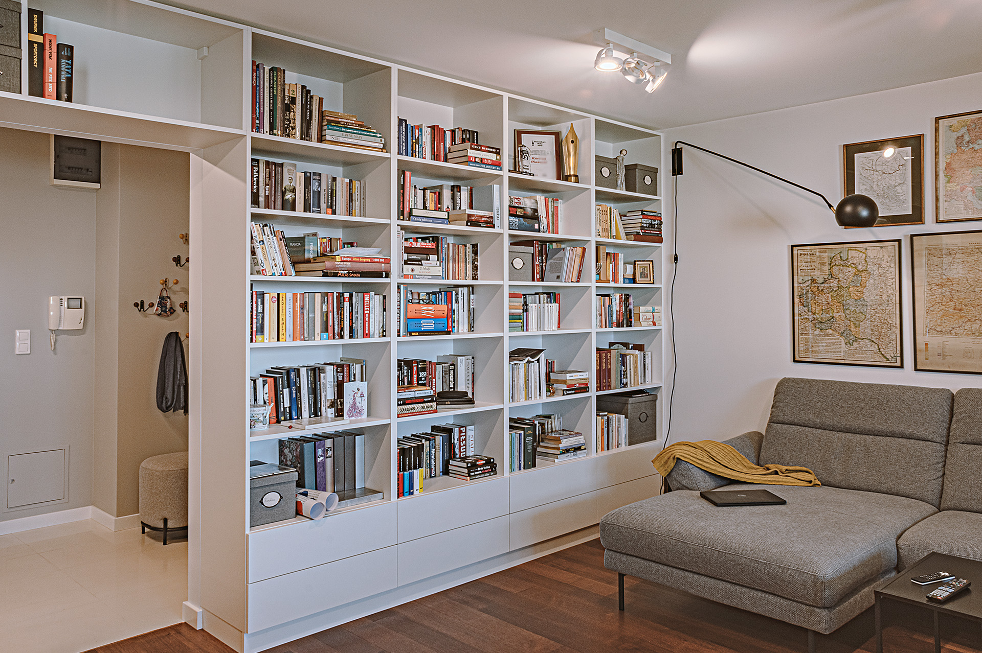 Głęboki regał na książki zajmuje całą wysokość i szerokość ściany na styku salonu z korytarzem, także nad otworem drzwiowym.